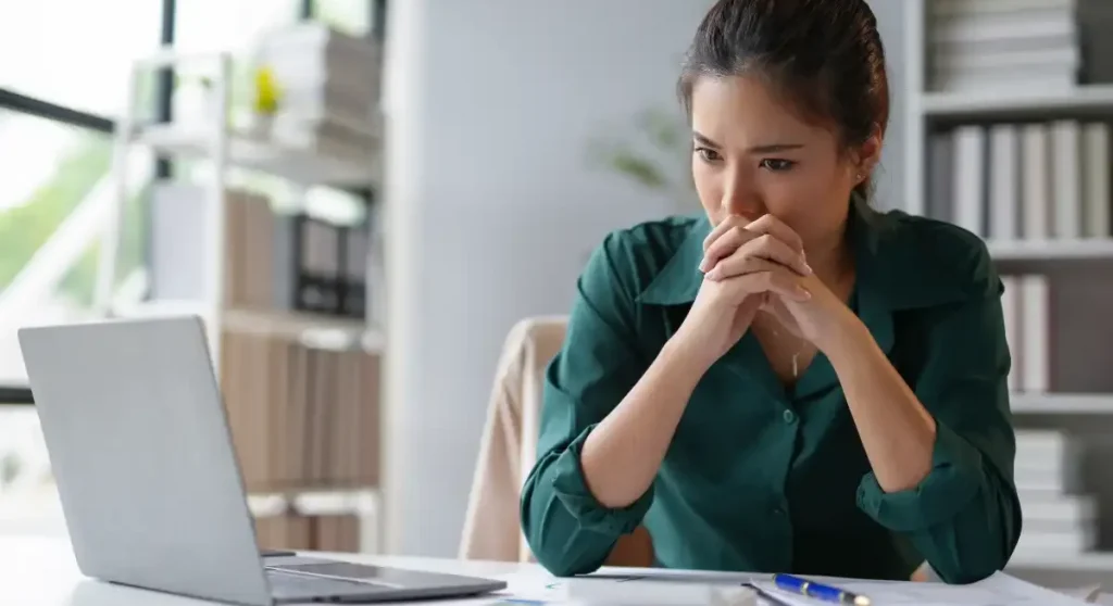 women wearing green shirt in office looking at computer deep in thought