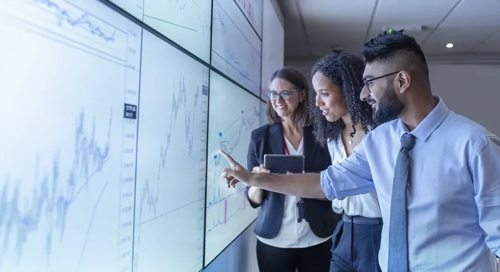Man pointing at graph on screen standing next to two women