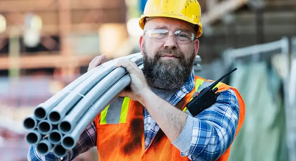 construction worker carrying steel tubes on construction site